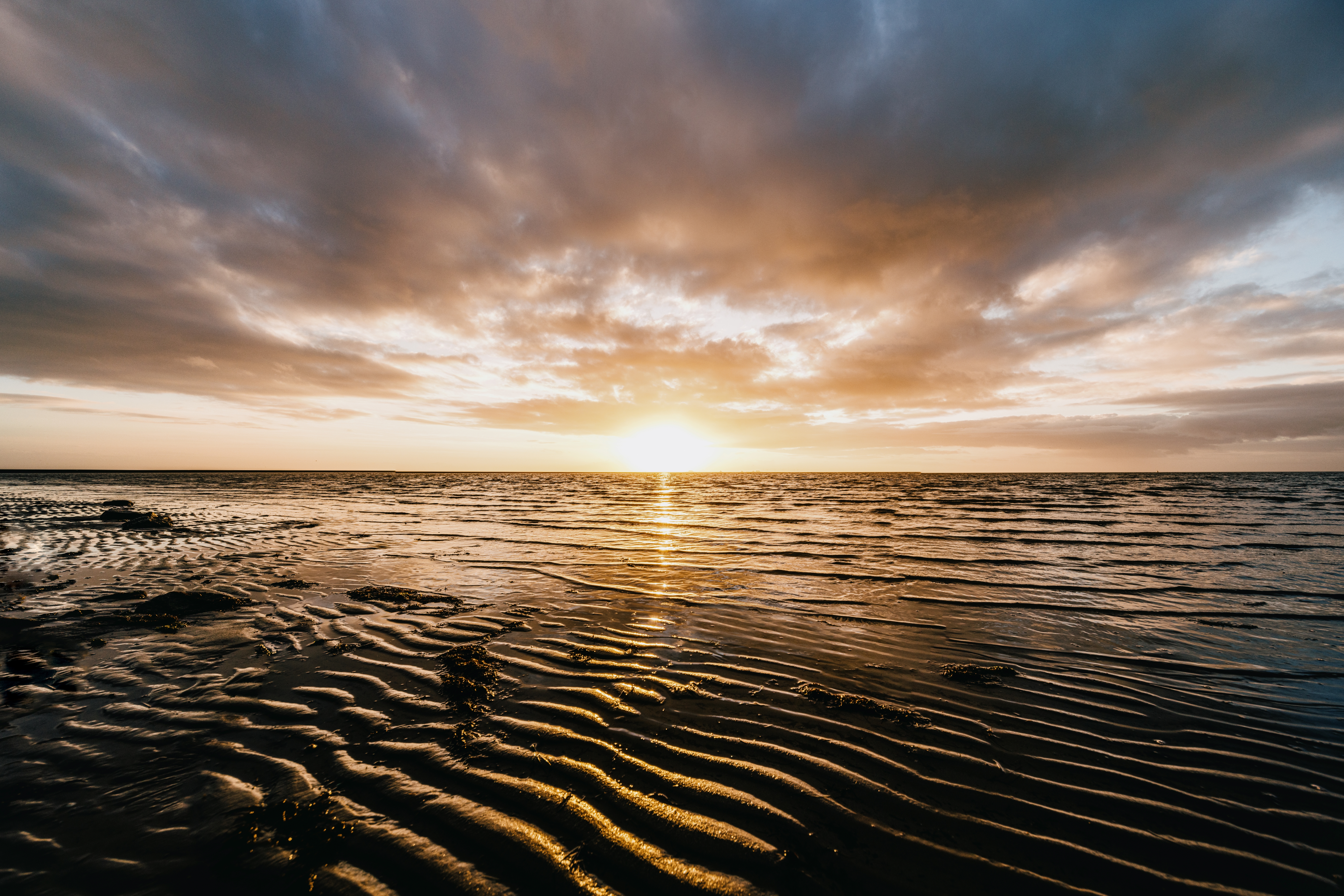 Die untergehende Sonne reflektiert auf dem Wattboden