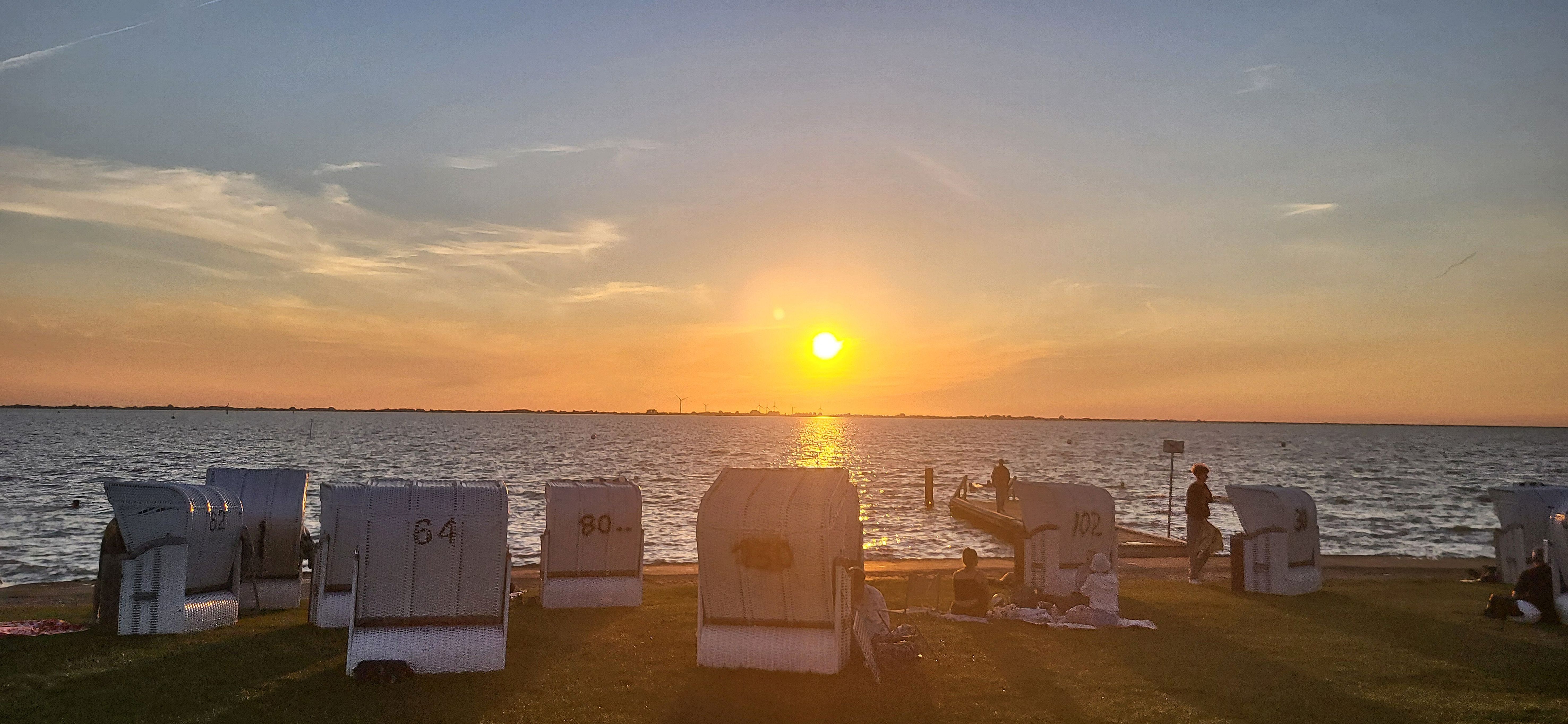 Blick über Strandkörbe hinweg auf den Sonnenuntergang an der Dockkoogspitze