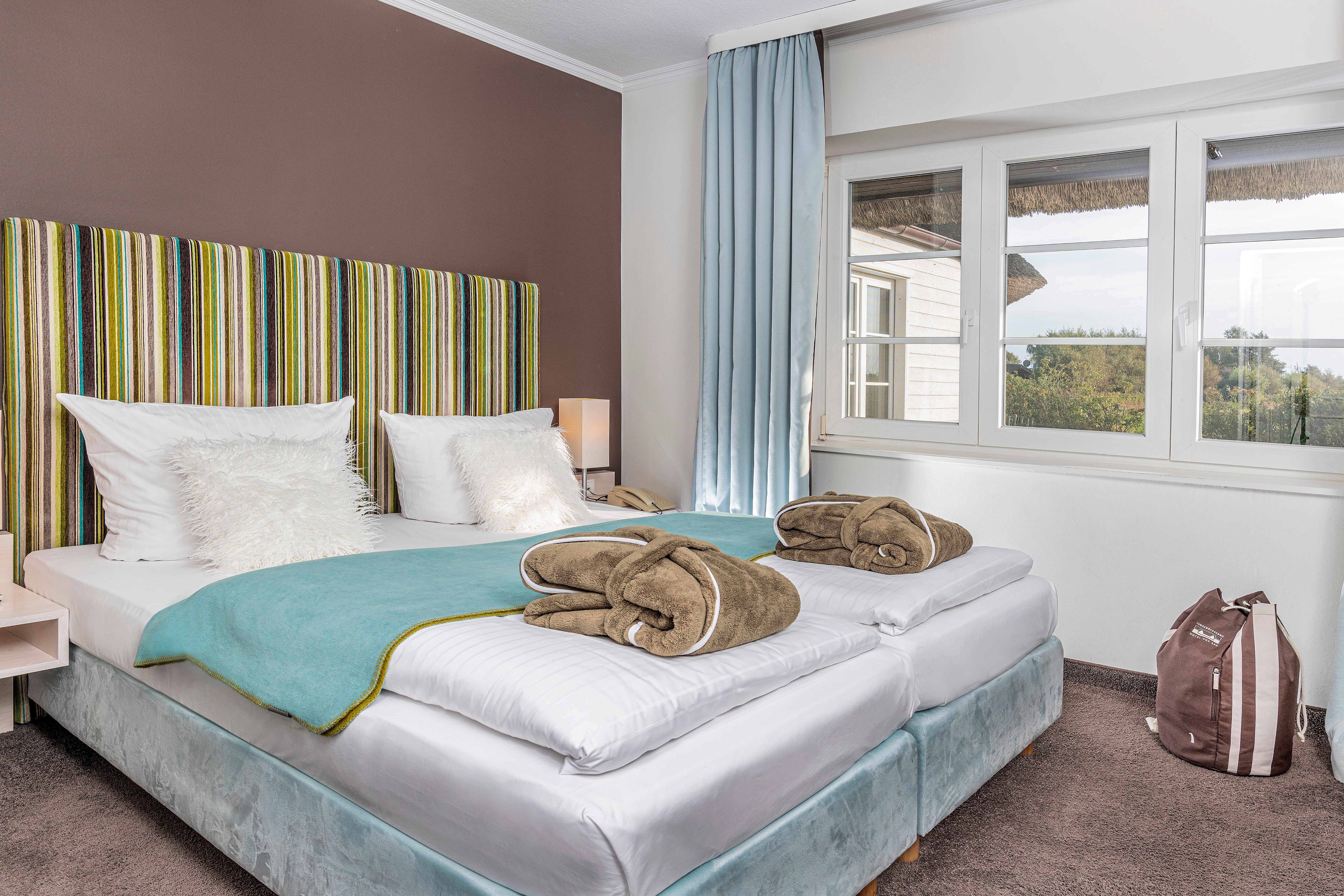 Ein kleines Doppelzimmer im Hotel mit Blick auf ein gemütliches Doppelbett und dem Ausblick auf die Außenanlage des Hotels aus dem Fenster