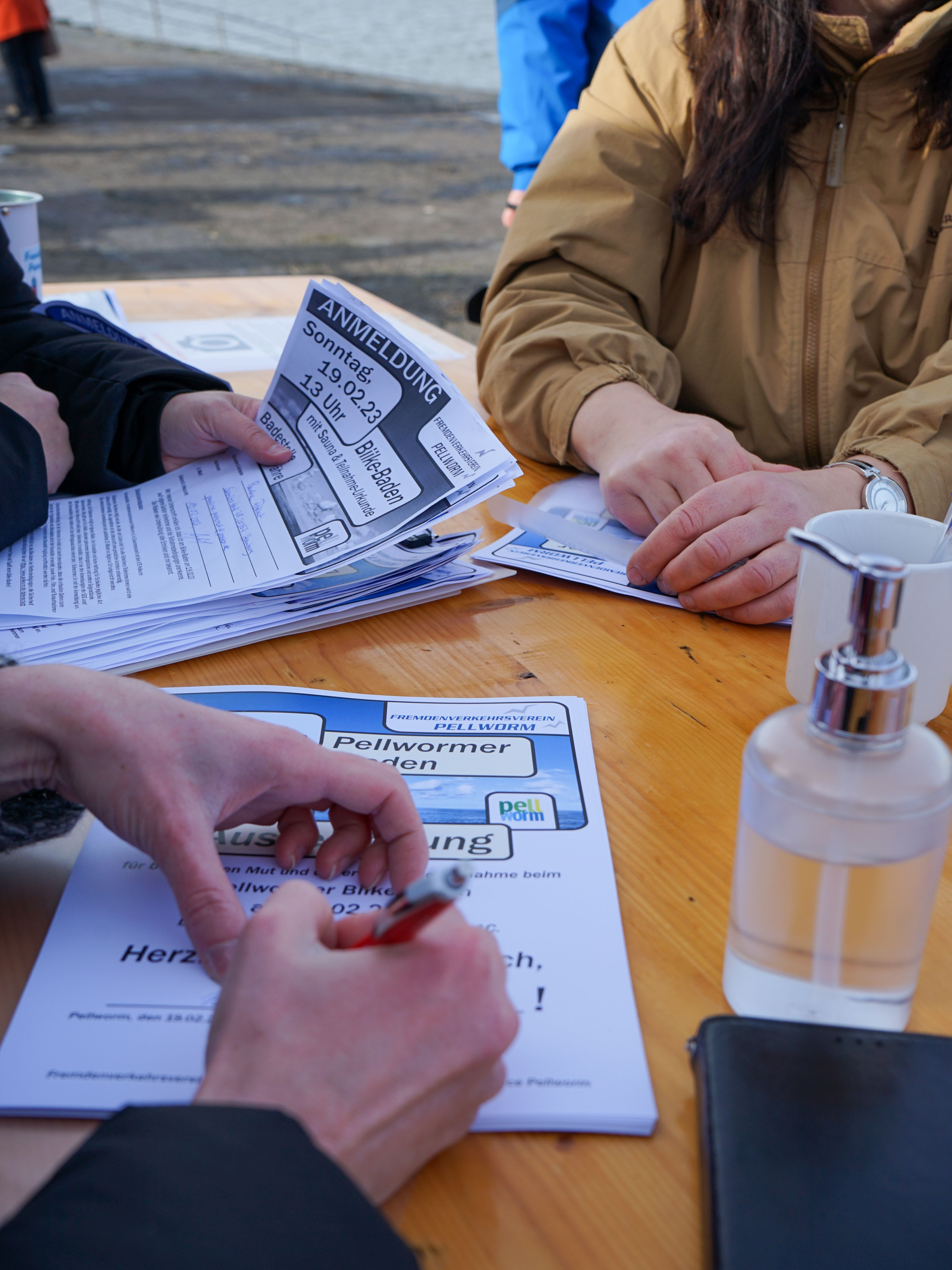 Personen füllen Anmeldeformulare für das Biikebaden auf Pellworm aus. Auf dem Tisch liegen Papiere und Stifte.