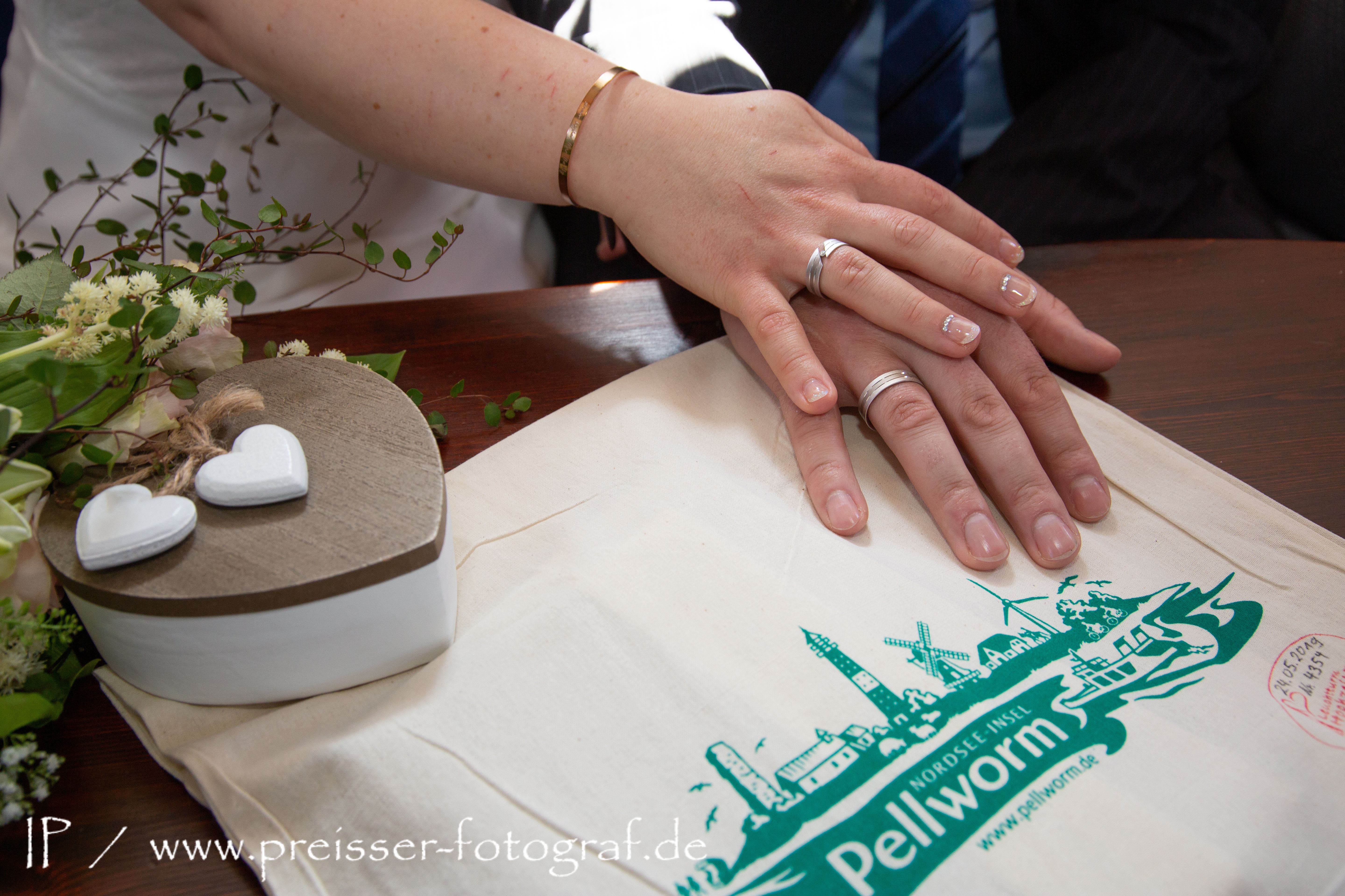 ein verheiratetes Paar legt seine Hände  auf ein Tischdeckchen, auf dem die Insel Pellworm abgebildet ist