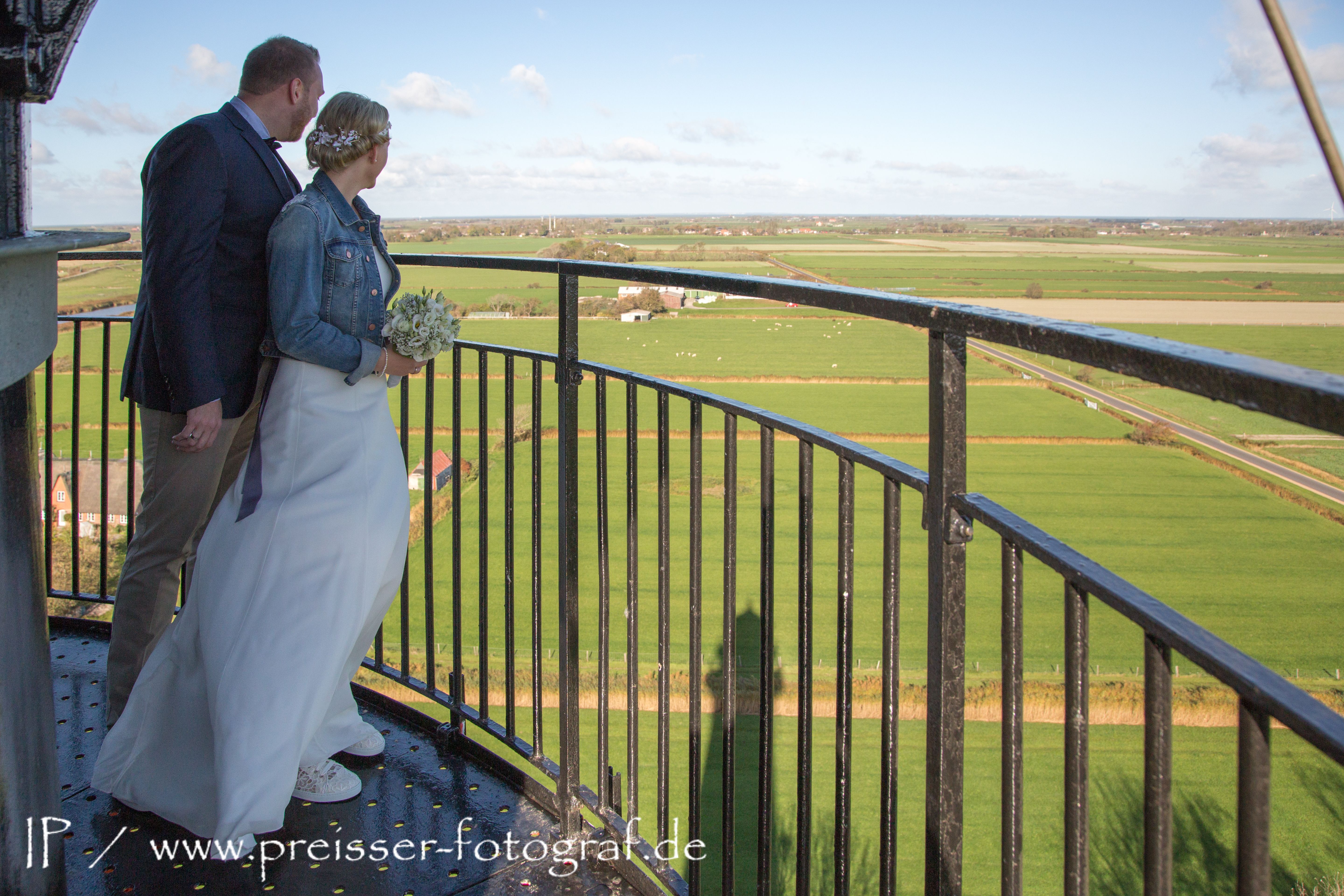 Ein Brautpaar steht auf dem Pellwormer Leuchtturm und schaut über Pellworms Landschaft